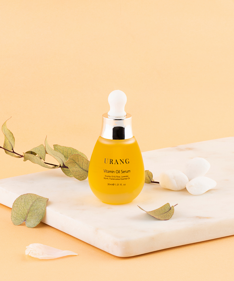 Bouteille de URANG Vitamin Oil Serum 30ml sur une table en marbre avec feuilles et pétales décoratifs.