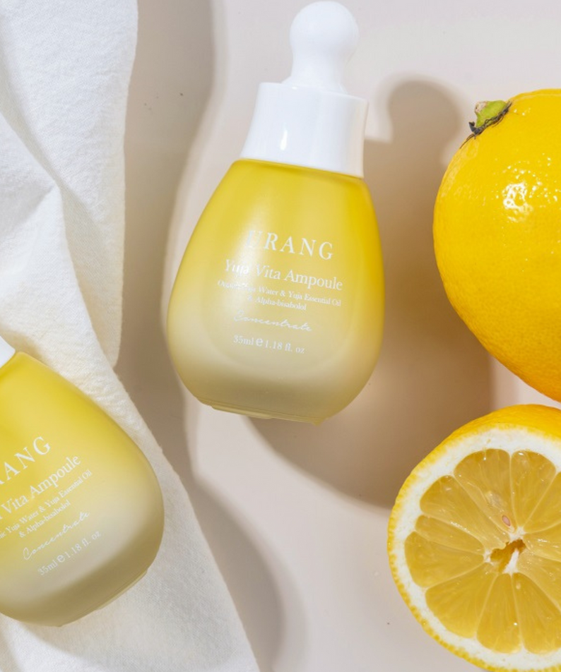 Flacons de URANG Yuja Vita Ampoule posés à côté de fruits frais, soulignant la richesse en vitamines de ce produit.