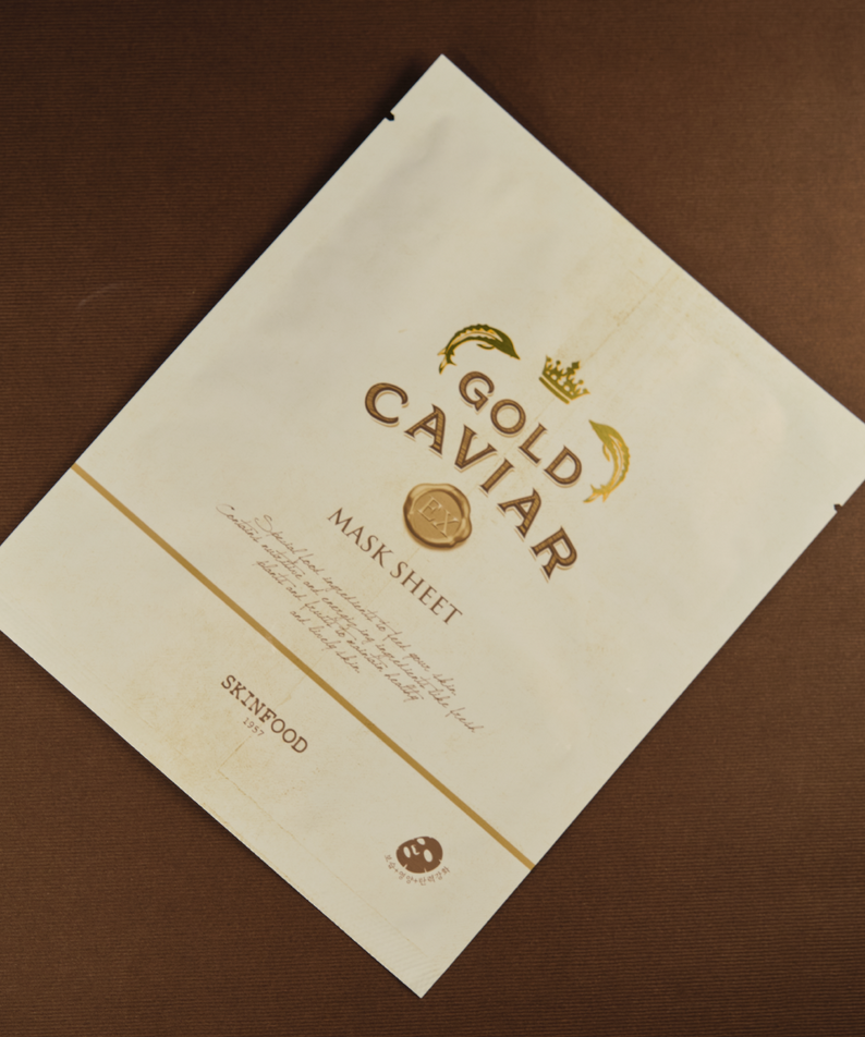 SKINFOOD Gold Caviar EX Mask Sheet : masque en feuille dorée sur fond brun, marque SKINFOOD, contexte visuel élégant.