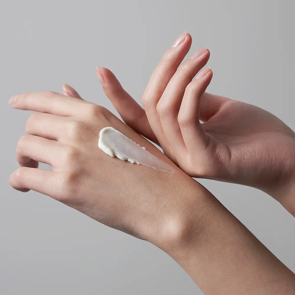 VIDIVICI The Cashmere Hand Treatments 50ml sur mains, crème blanche appliquée, mains soignées sur fond gris clair.