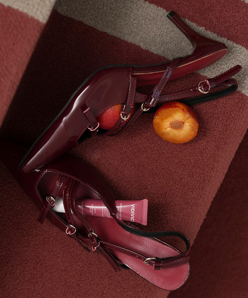 Talons hauts bordeaux avec VIDIVICI Peptide Butter Tint Balm et une prune sur un tapis rouge foncé.