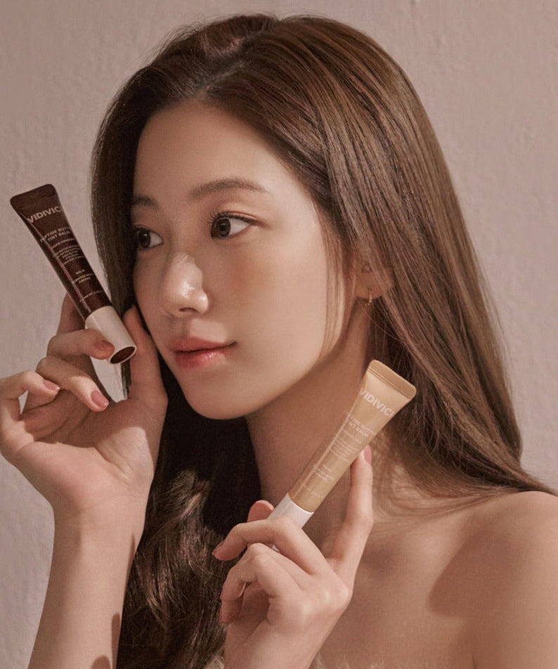 Femme tenant VIDIVICI Peptide Butter Tint Balm en regardant sur le côté, maquillage naturel et élégant.