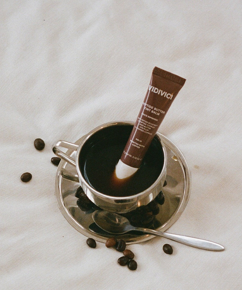 Produit cosmétique VIDIVICI Peptide Butter Tint Balm sur une tasse de café avec grains, esthétique et élégant.
