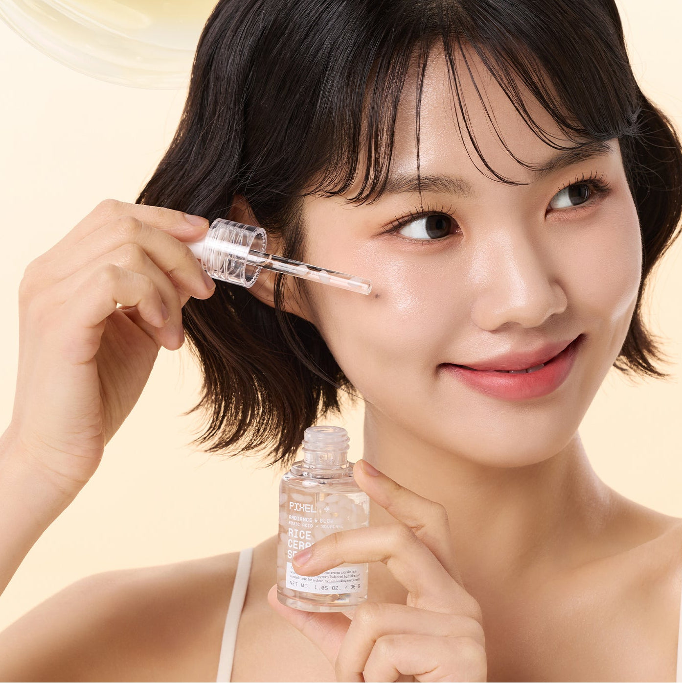 Décris l'image en français : VT COSMETIC Rice Ceramide Serum 30ml, marque VT, sur flacon et pipette près du visage d’une femme.