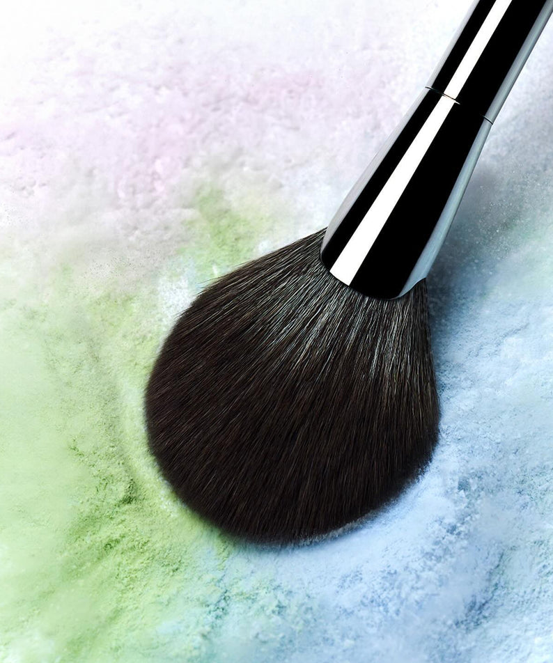 Pinceau appliquant WAKE MAKE Stay Fixer Multi Color Powder 4g sur fond texturé coloré.