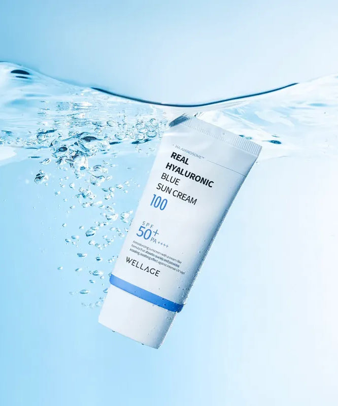 WELLAGE  Real Hyaluronic Blue Sunscreen 50ml : tube bleu sur peau, gouttelettes d’eau, visuel rafraîchissant.
