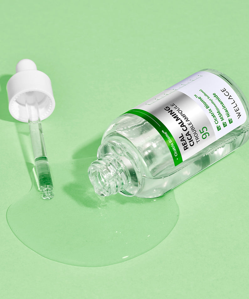 Flacon renversé de WELLAGE Real Cica Calming 95 Trouble Ampoule 50ml sur un fond vert, avec une pipette à côté.