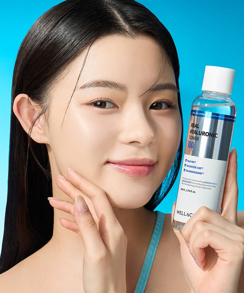 Femme souriante tenant WELLAGE Real Hyaluronic 100 Toner 200ml à côté de son visage, éclairage lumineux, fond bleu.