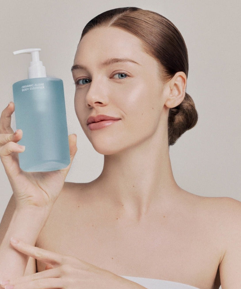 WHAMISA Organic Algae Fermented Body Cleanser 490ml, marque WHAMISA, femme montrant le flacon bleu en salle de bain.