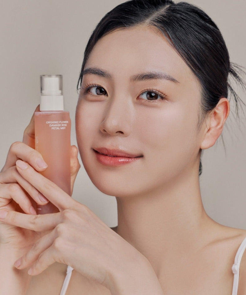 WHAMISA Organic Flower Fermented Rose Petal Mist 100ml, femme tenant le spray visage au fond clair, ambiance beauté.