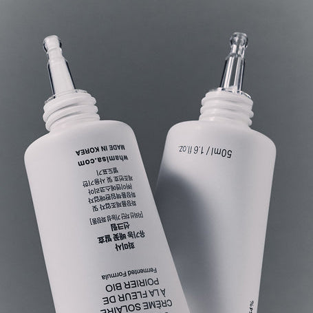 Décris l'image en français : WHAMISA Organic Pear Blossom Fermented Sunscreen 50ml de la marque WHAMISA, flacons sur fond gris.