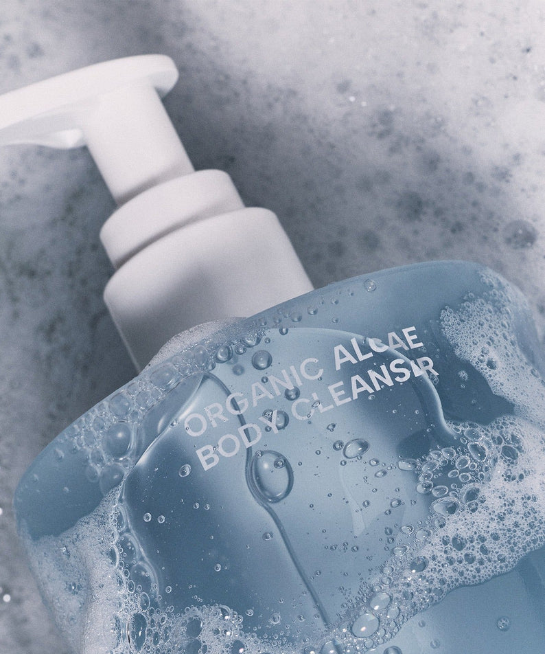 Flacon du WHAMISA Organic Algae Fermented Body Cleanser 490ml avec mousse sur fond de bulles.