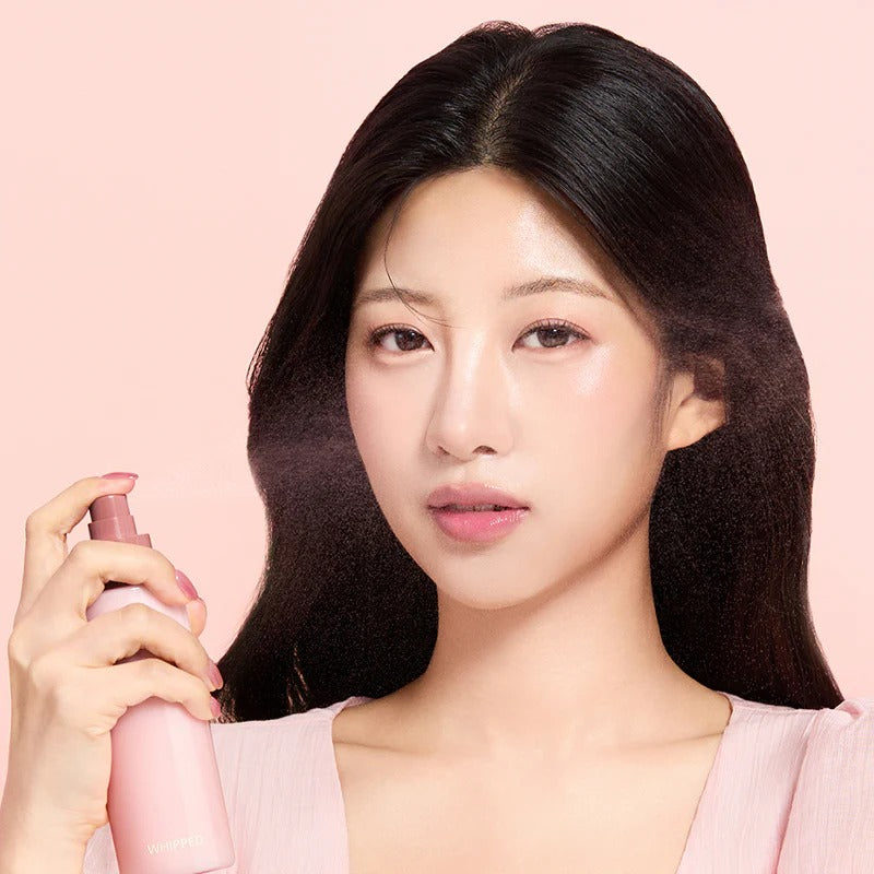 WHIPPED Butter Vegan Milk Foam Pack Mist 150ml, flacon rose tenu par une femme sur fond rose, marque WHIPPED.