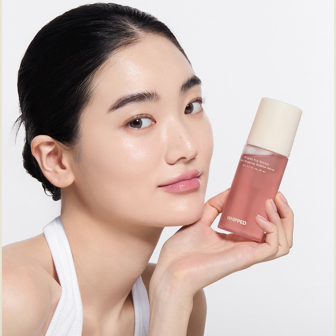 WHIPPED Butter Vegan Whipping Bubble Serum 92ml sur peau éclatante, femme en studio tenant le flacon rose.