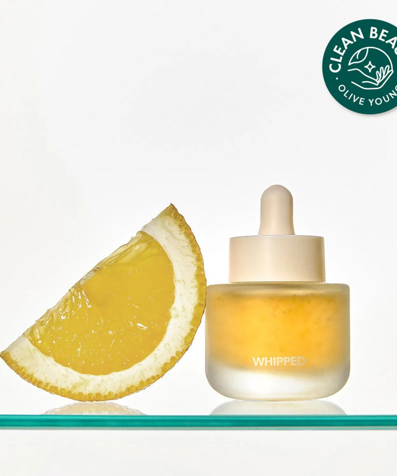 Flacon de 30ml de WHIPPED Yujamong Vegan Vita Syrup Ampoule à côté d'une tranche de citron, avec un label "Clean Beauty Olive Young".