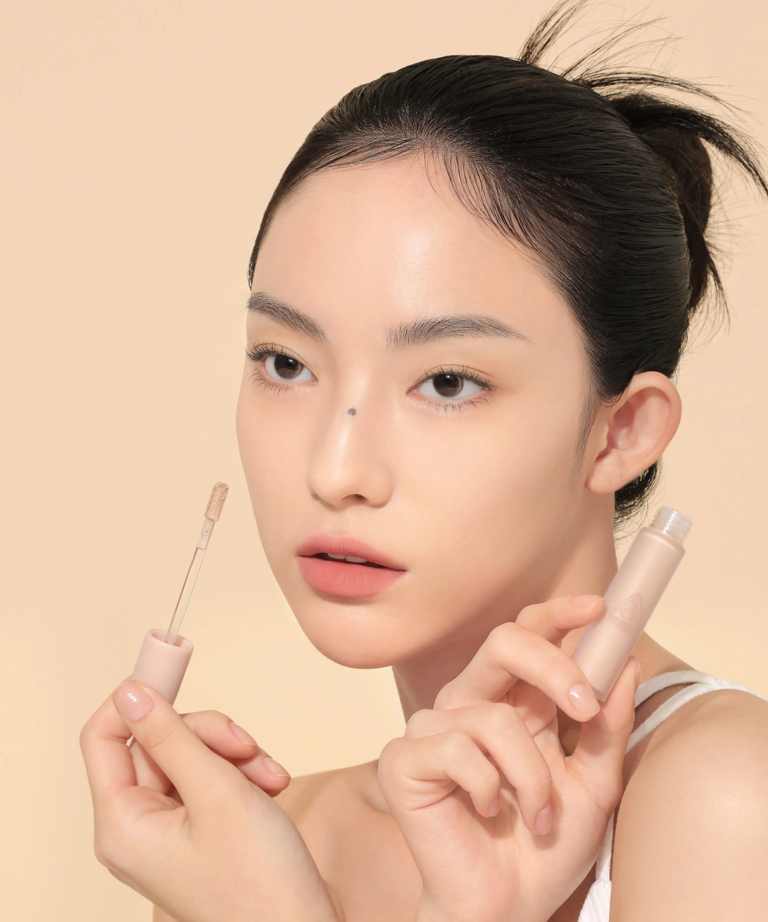 Portrait maquillage : 3CE Skin Fit Cover Liquid Concealer de 3CE, application sous les yeux sur fond beige.