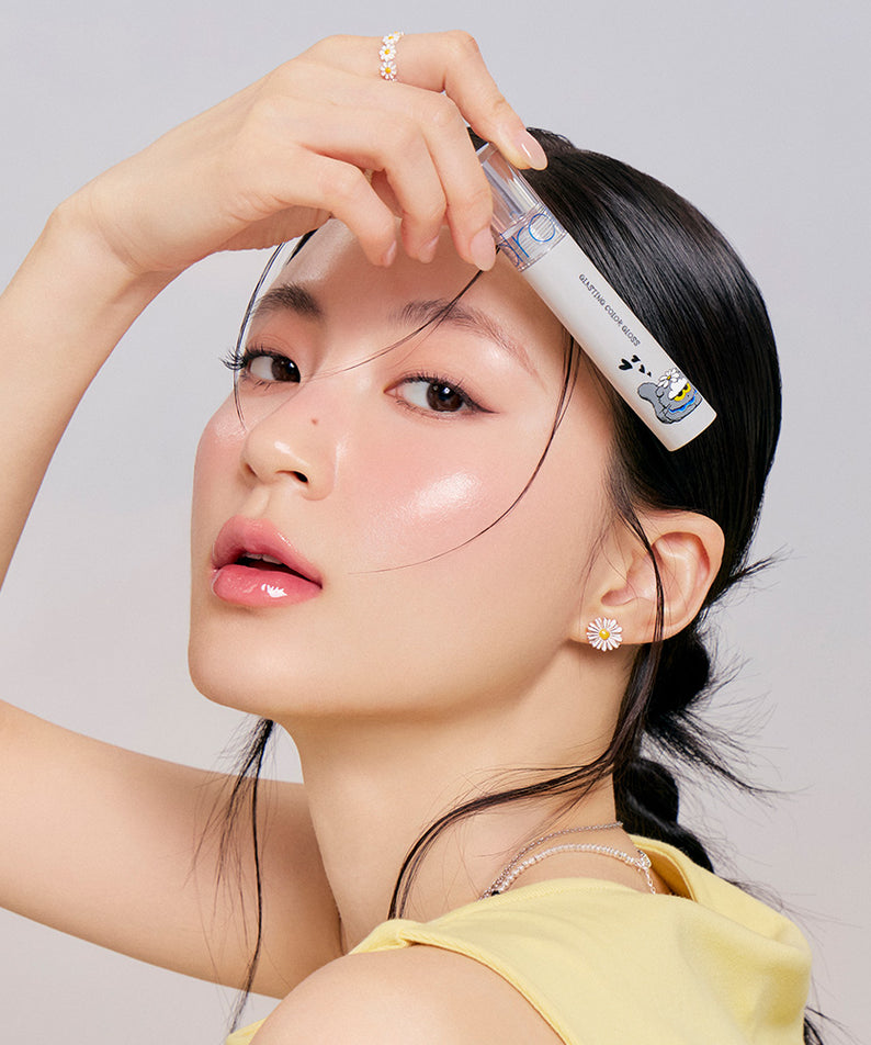 Femme portant ROMAND x Joanne Friends Glasting Color Gloss avec éclat, présentant le produit près de son visage.