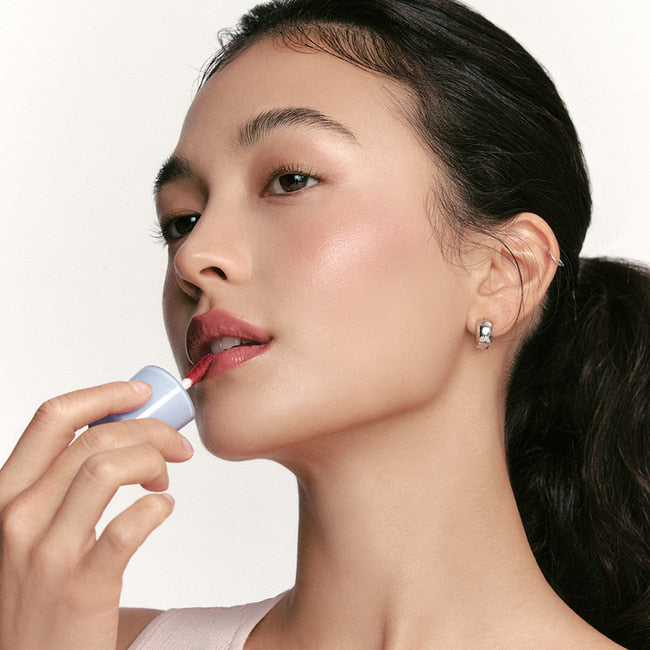 NUSE Care Liptual sur lèvres, femme applique un baume, fond clair, marque NUSE Care Liptual en gros plan