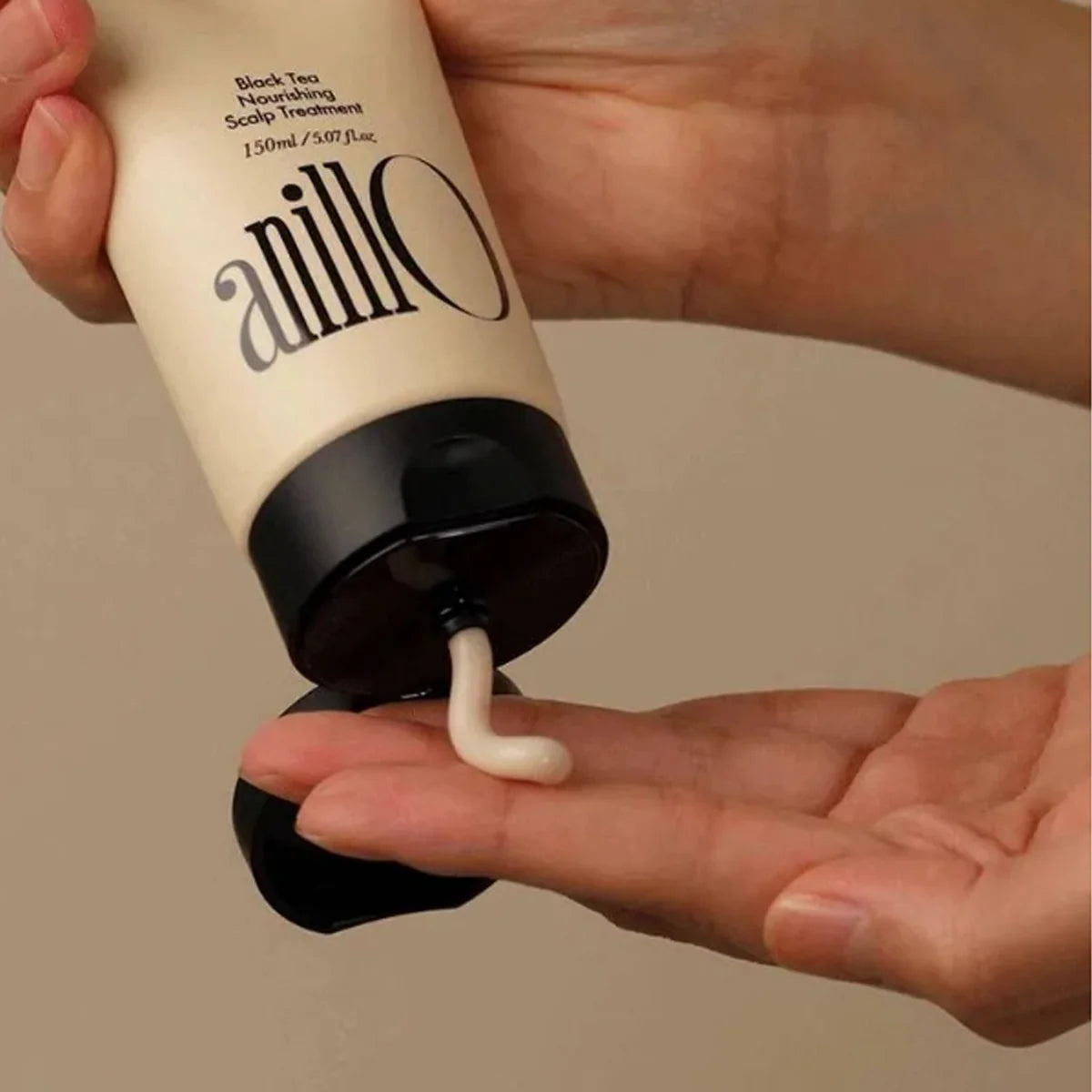 Décris l'image en français : ANILLO Black Tea Nourishing Scalp Treatment 150ml, tube tenu par une main, crème appliquée sur cuir chevelu.