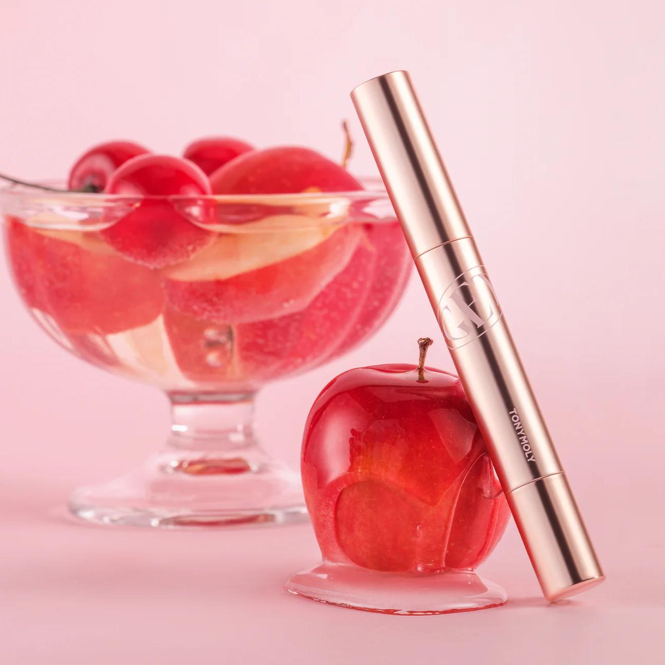 TONY MOLY Get It Tint Glaze Balm, tube doré sur fond rose, baies rouges en arrière-plan—produit de maquillage.