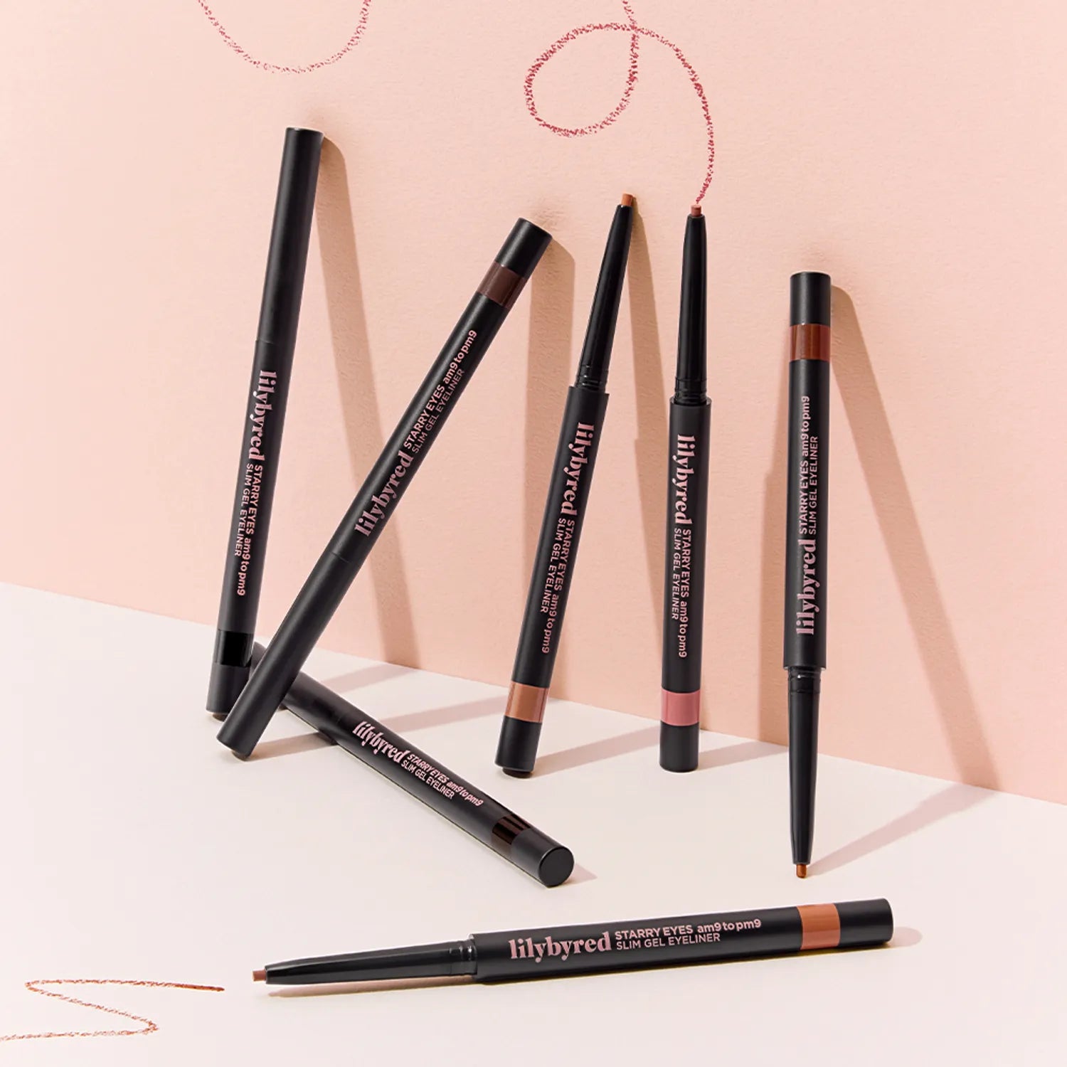 LILYBYRED Starry Eyes 9 to 9 Slim Gel Eyeliner : stylos eyeliner sur fond rose, swirls de maquillage en décor.