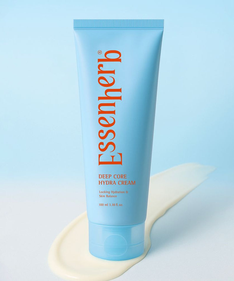 Crème hydratante ESSENHERB Deep Core Hydra Cream 100ml en tube bleu, posée sur fond bleu et éclaboussée de crème.