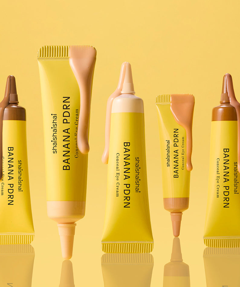 SHAISHAISHAI Banana PDRN Conceal Eye Cream 15ml, tubes jaunes sur fond jaune en contexte maquillage beauté.