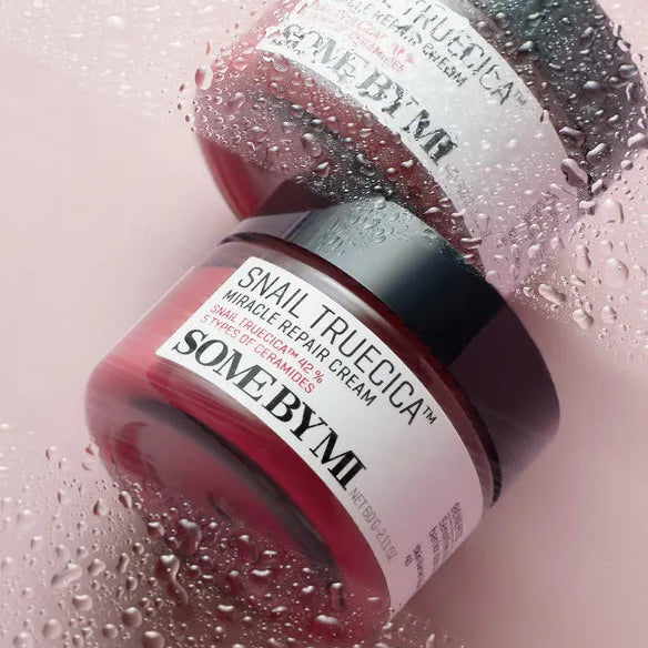 SOME BY MI Snail Truecica Miracle Repair Cream 60g, crème SOME BY MI sur fond rose, gouttes d’eau, flacon visible