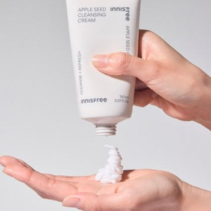 INNISFREE Apple Seed Cleansing Cream 150ml : tube de crème sur peau, main appliquant une texture blanche, fond clair.