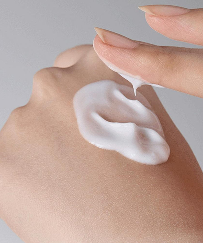 INNISFREE Olive Vitamin E Real Lotion 170ml sur peau avec crème, main appliquant le produit, fond clair.