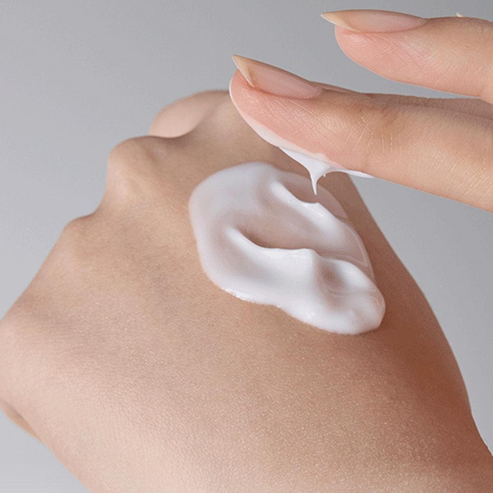 INNISFREE Olive Vitamin E Real Lotion 170ml sur peau avec crème, main appliquant le produit, fond clair.