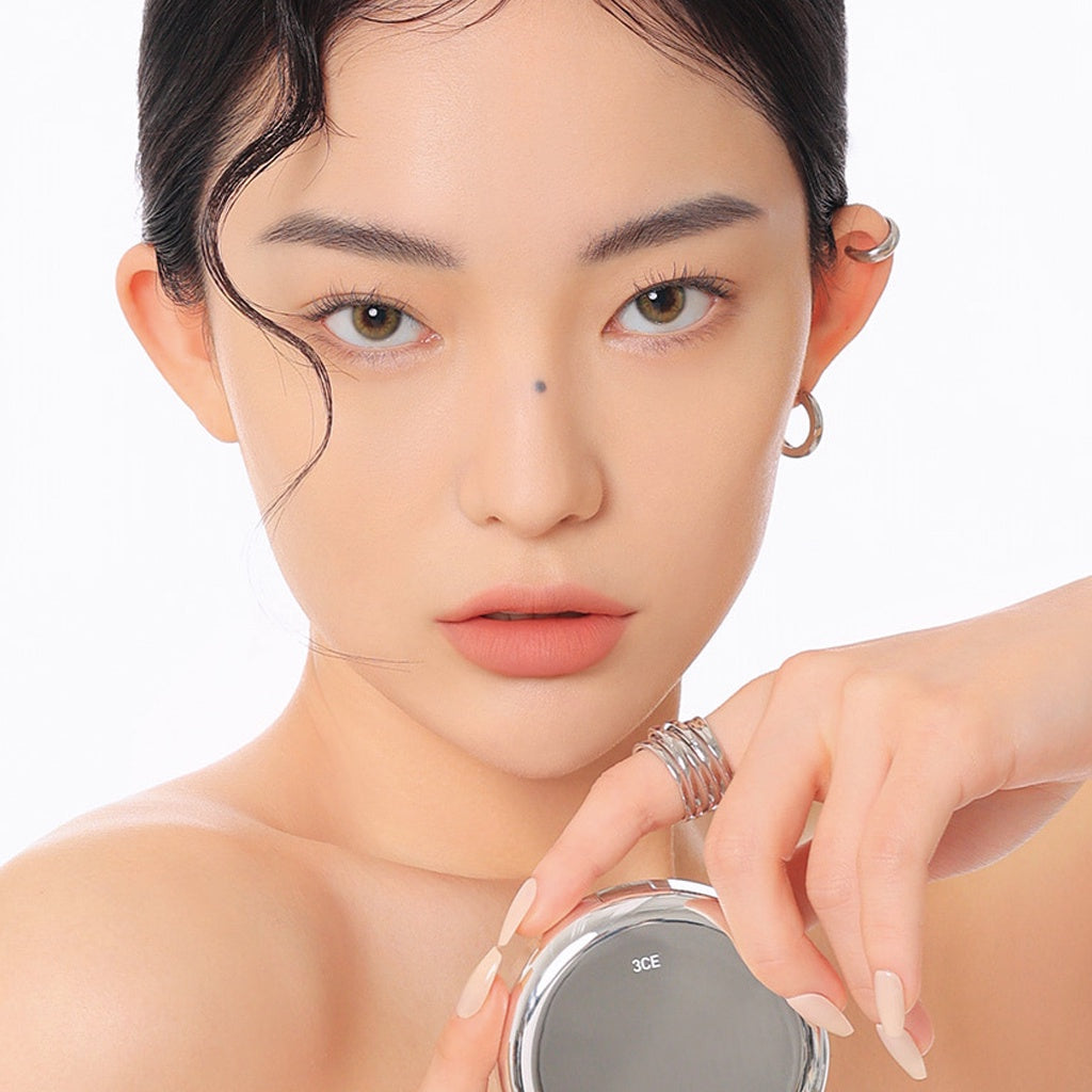 Décris l'image en français avec 3CE  Makeup Fix Powder 9g : poudre fixatrice 3CE sur une femme maquillée, fond blanc, gros plan.