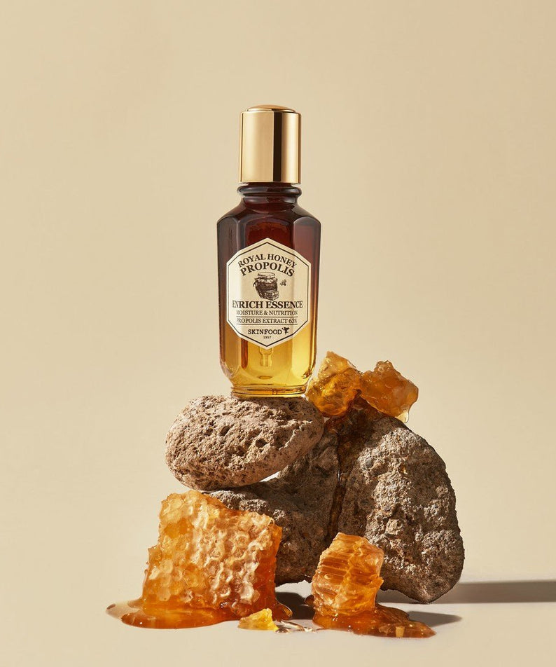 SKINFOOD Royal Honey Propolis Enrich Essence 50ml, bouteille SKINFOOD sur fond beige avec miel et pierre dorée, photo produit