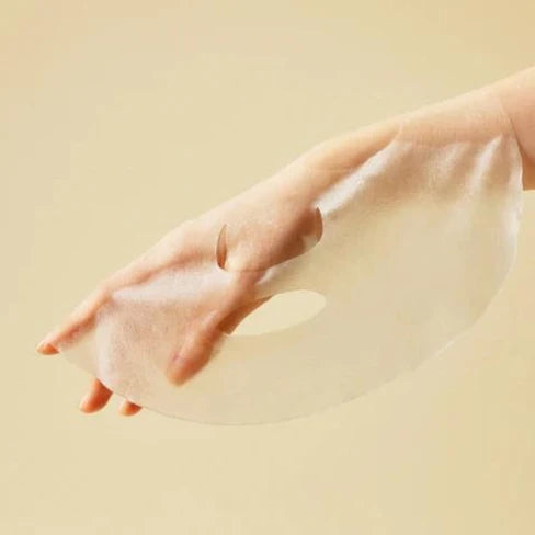 SOME BY MI Yuja Niacin Blemish Care Serum Sheetmask : masque visage en tissu jaune, main tenant le produit sur fond beige.