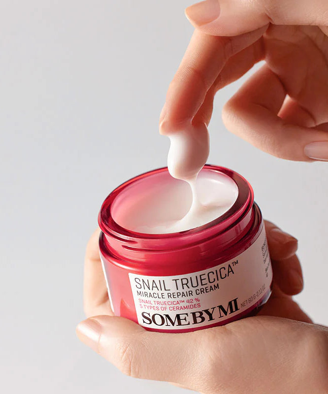 SOME BY MI Snail Truecica Miracle Repair Cream 60g, pot rouge ouvert, crème blanche appliquée, main tenant.