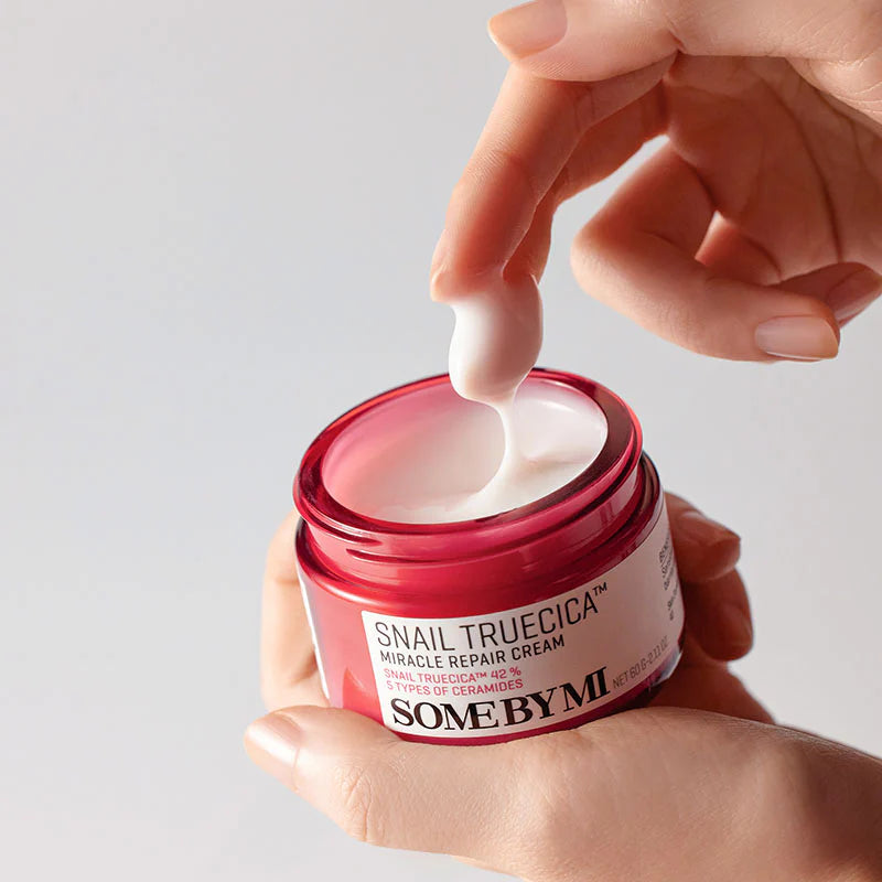 SOME BY MI Snail Truecica Miracle Repair Cream 60g, pot rouge ouvert, crème blanche appliquée, main tenant.