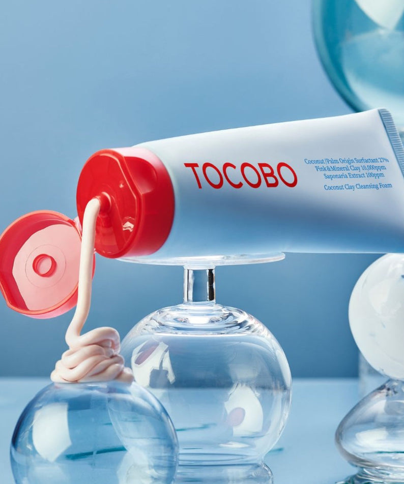 TOCOBO  Coconut Clay Cleansing Foam, tube rouge sur fond bleu, contexte cosmétique avec flacons et capuchon ouvert