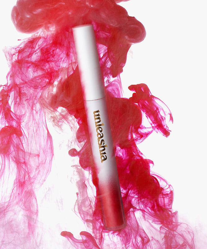 UNLEASHIA Luv Hug Velvet Tint de la marque UNLEASHIA, tube maquillage rouge sur fond blanc, fumée rose visuelle.