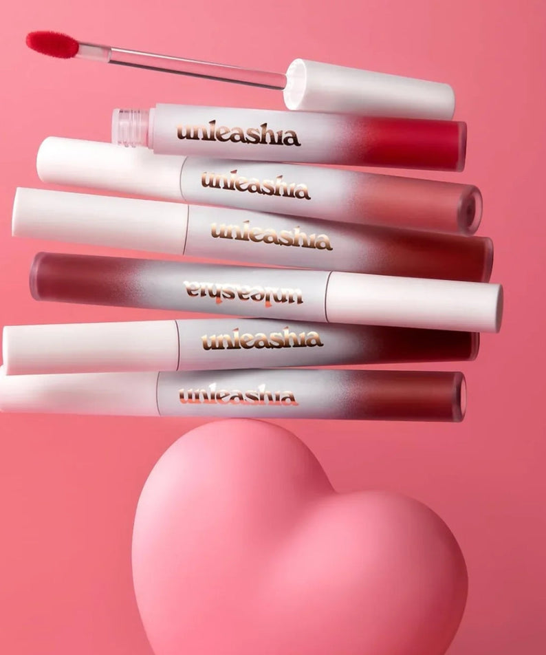UNLEASHIA Luv Hug Velvet Tint, rouges à lèvres velours de la marque UNLEASHIA, présentés sur fond rose en cœur.