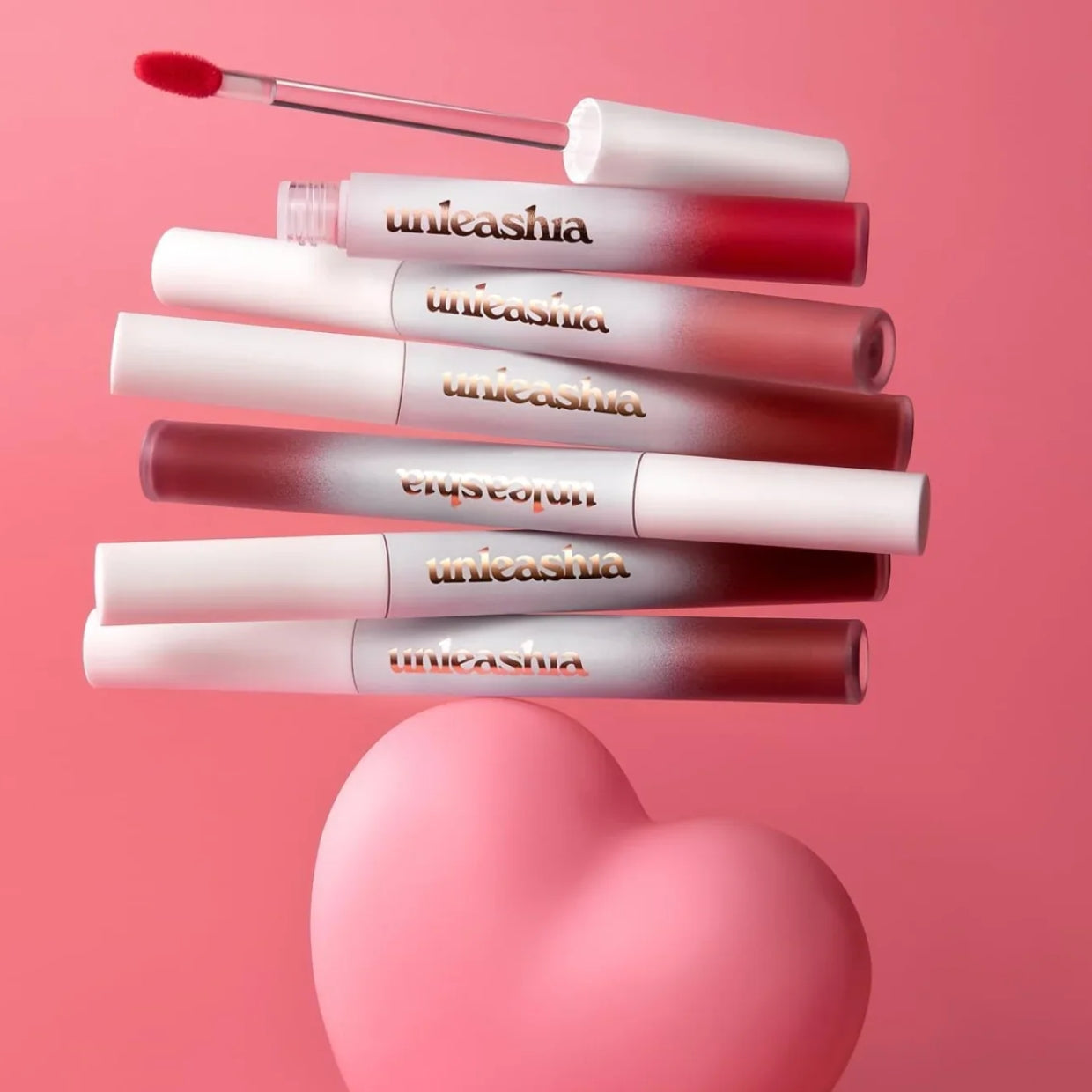 UNLEASHIA Luv Hug Velvet Tint, rouges à lèvres velours de la marque UNLEASHIA, présentés sur fond rose en cœur.
